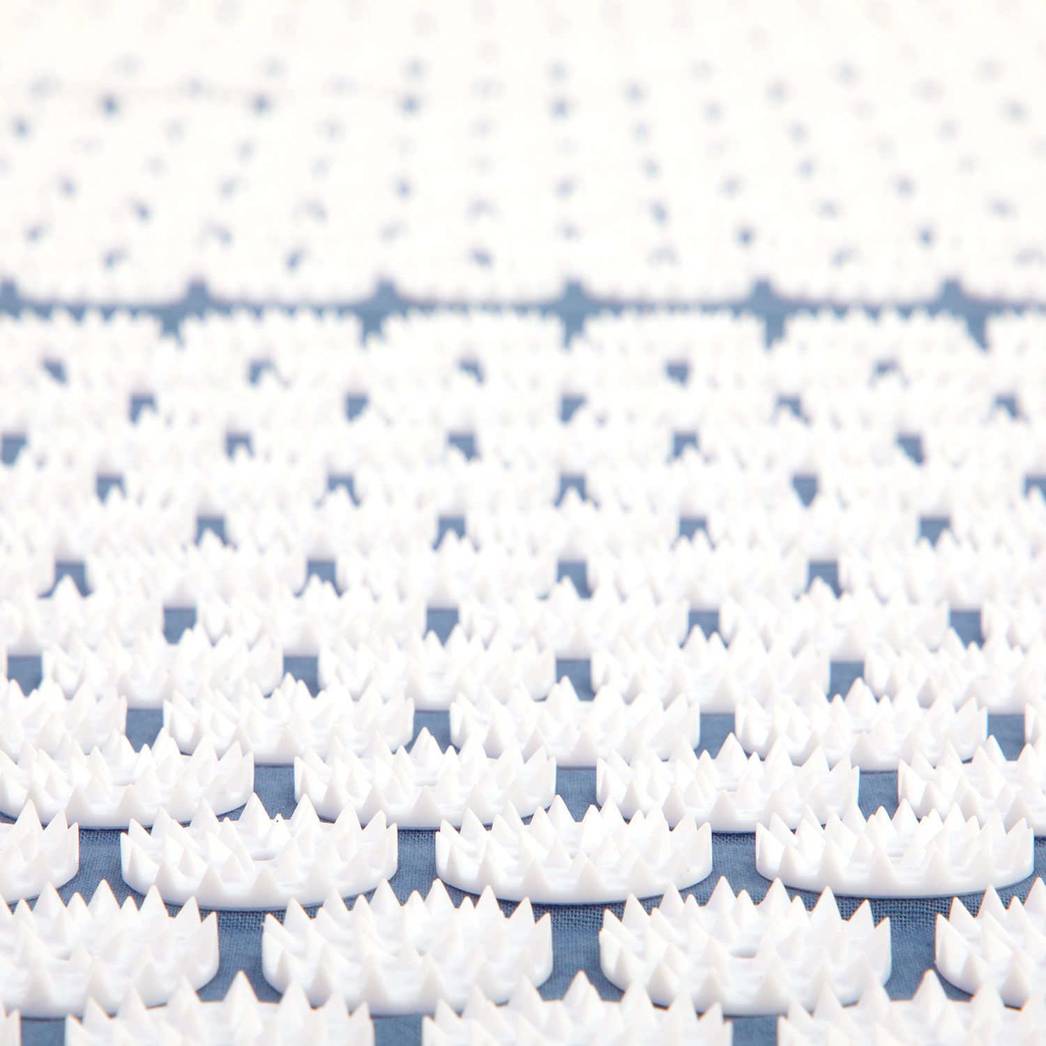 Gros plan des picots blancs sur un tapis d'acupression bleu. Les picots sont pointus et densément disposés.