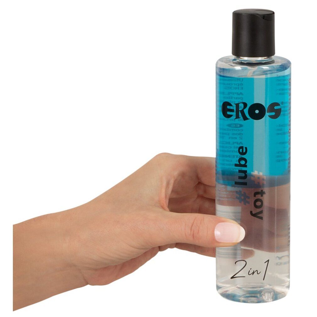 Main tenant une bouteille. Inscription: EROS, #lube, #toy, 2en1. Bouchon noir, liquide transparent.