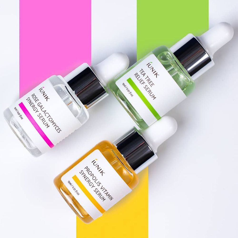 Trois flacons de sérum avec pipettes. Couleurs: rose, vert, jaune. Texte: iUNIK, Rose, Tea Tree, Propolis. Sur fond coloré.