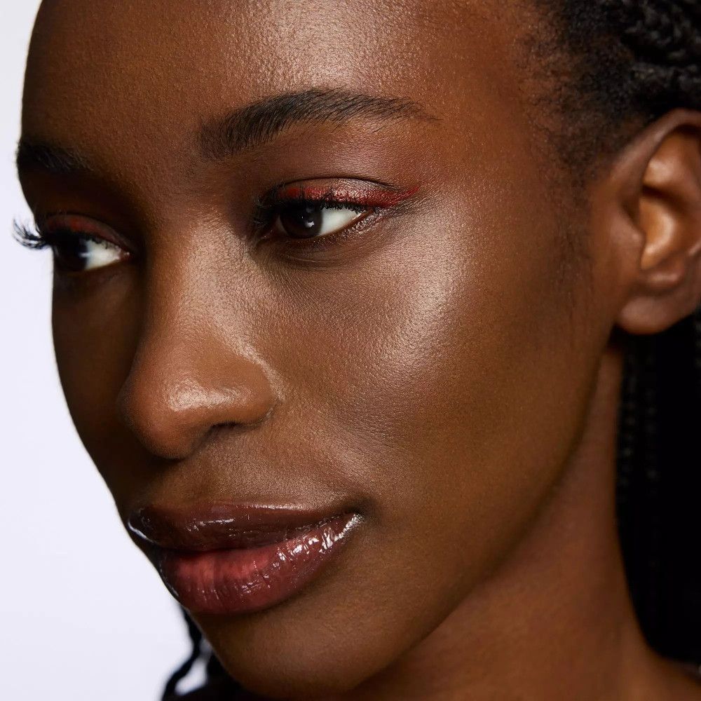 Gros plan sur une femme avec un trait d'eyeliner rouge. Lèvres brillantes.