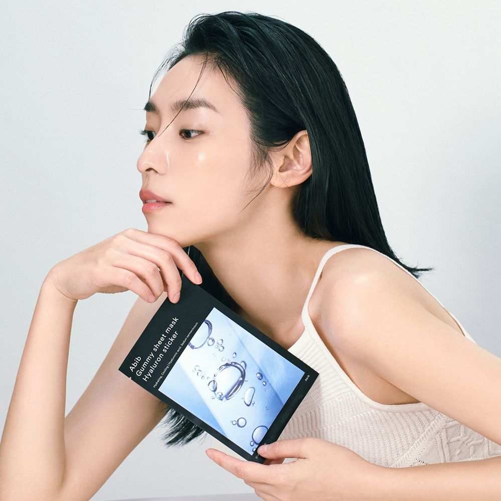 Personne tenant un emballage noir avec nom du produit et ingrédients. La personne porte un débardeur.