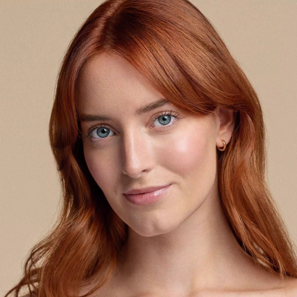 Portrait d'une femme aux cheveux roux et aux yeux bleus. Elle porte du maquillage.