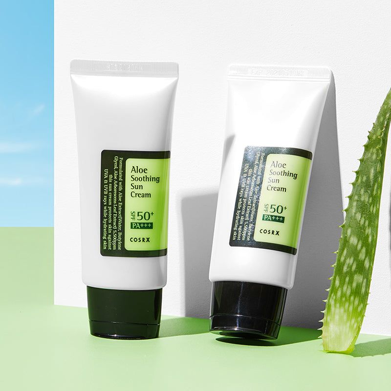 Twee witte tubes met zwarte dop. Etiketten met productinformatie. Tekst: Aloe Soothing Sun Cream SPF50+ PA+++. Aloëblad.