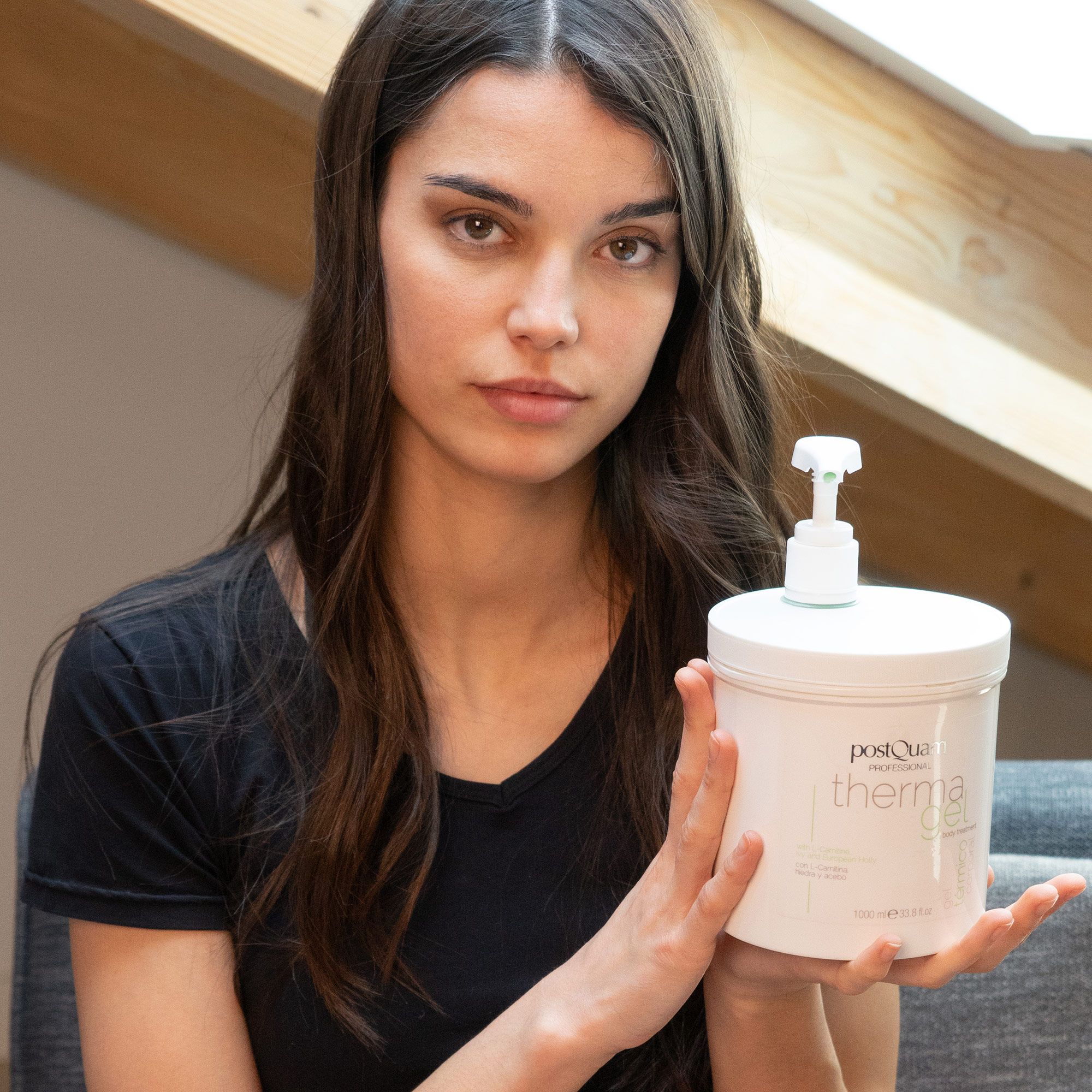 Vrouw houdt witte pot 'PostQuam therma gel' met pomp. Draagt zwart topje.