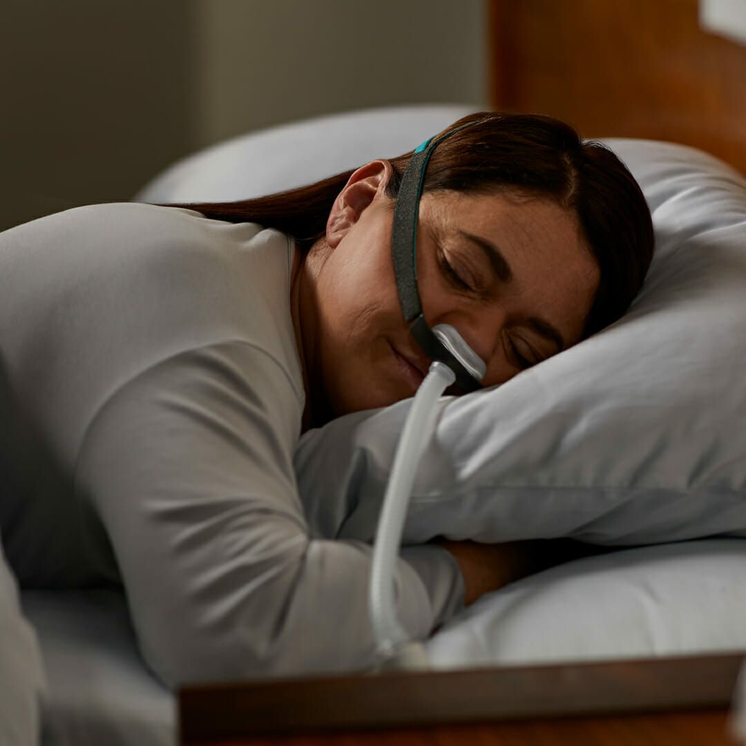Vrouw slaapt met CPAP-neusmasker op kussen.