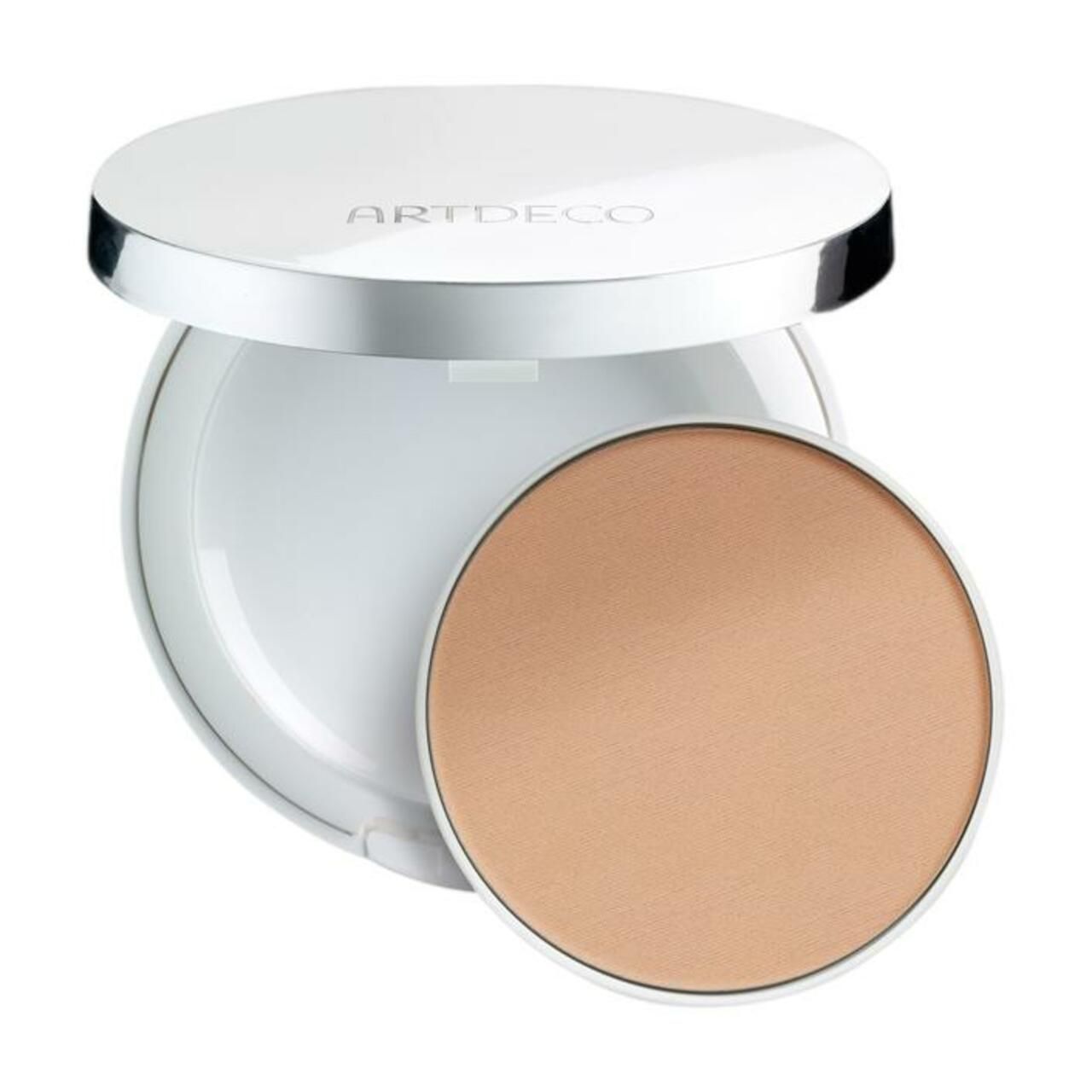 Witte compactpoeder met zilveren rand en opschrift ARTDECO. Open doosje met beige poeder. Ronde vorm.