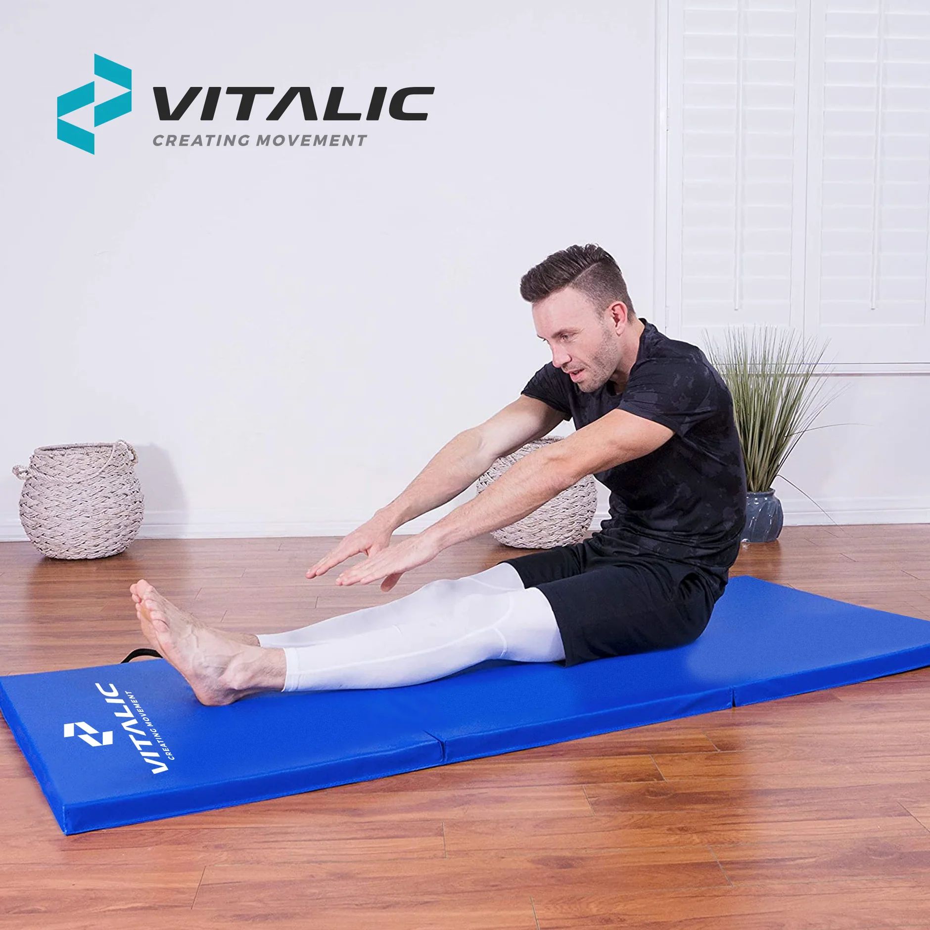 Man zit op blauw gymnastiekmat en rekt zich uit. Logo zichtbaar. Op houten vloer.