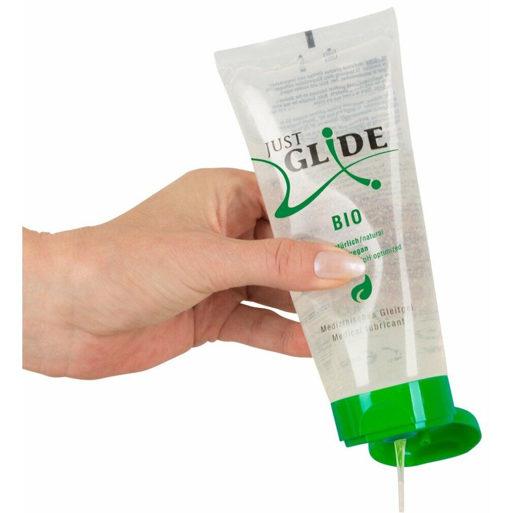 Main tenant un tube transparent avec bouchon vert. Inscription: JUST GLIDE BIO. Lubrifiant sortant du tube.
