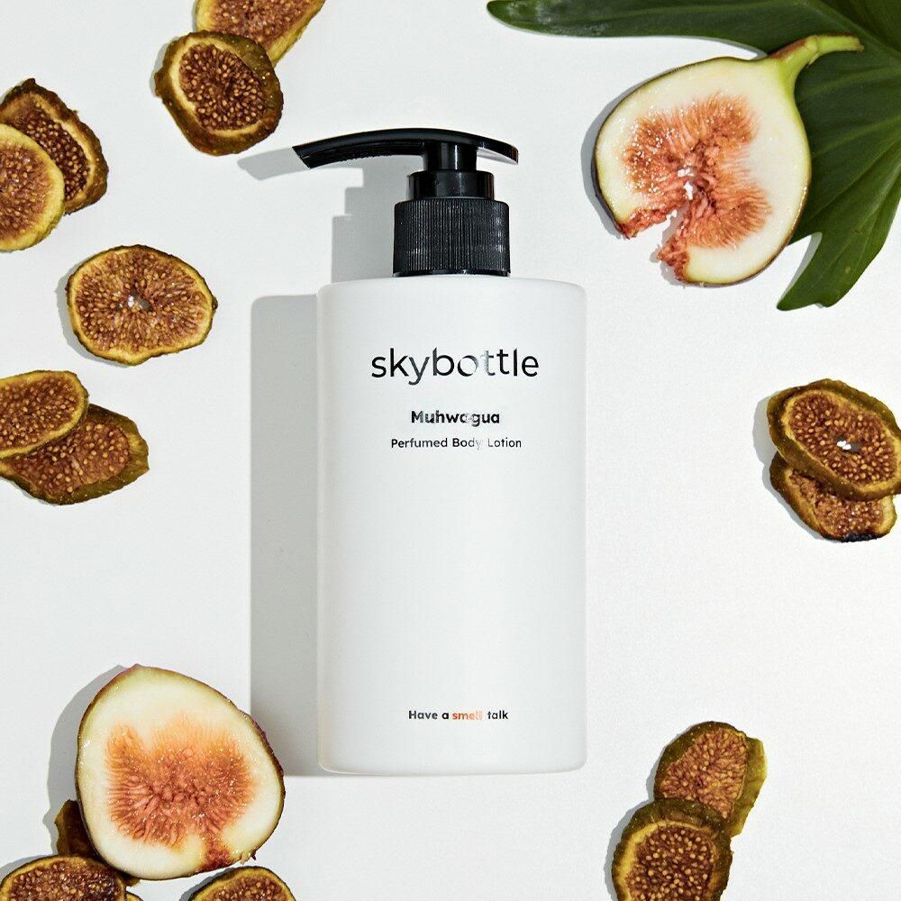Witte fles met zwarte pomp, omringd door vijgen en gedroogde vijgenschijfjes. Opschrift: skybottle, Muhwagua Perfumed Body Lotion.