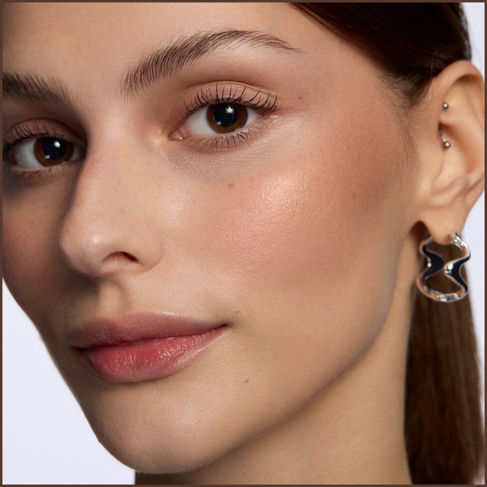 Gros plan sur un visage. Femme aux yeux bruns, boucle d'oreille. Peau maquillée. Lumière naturelle.