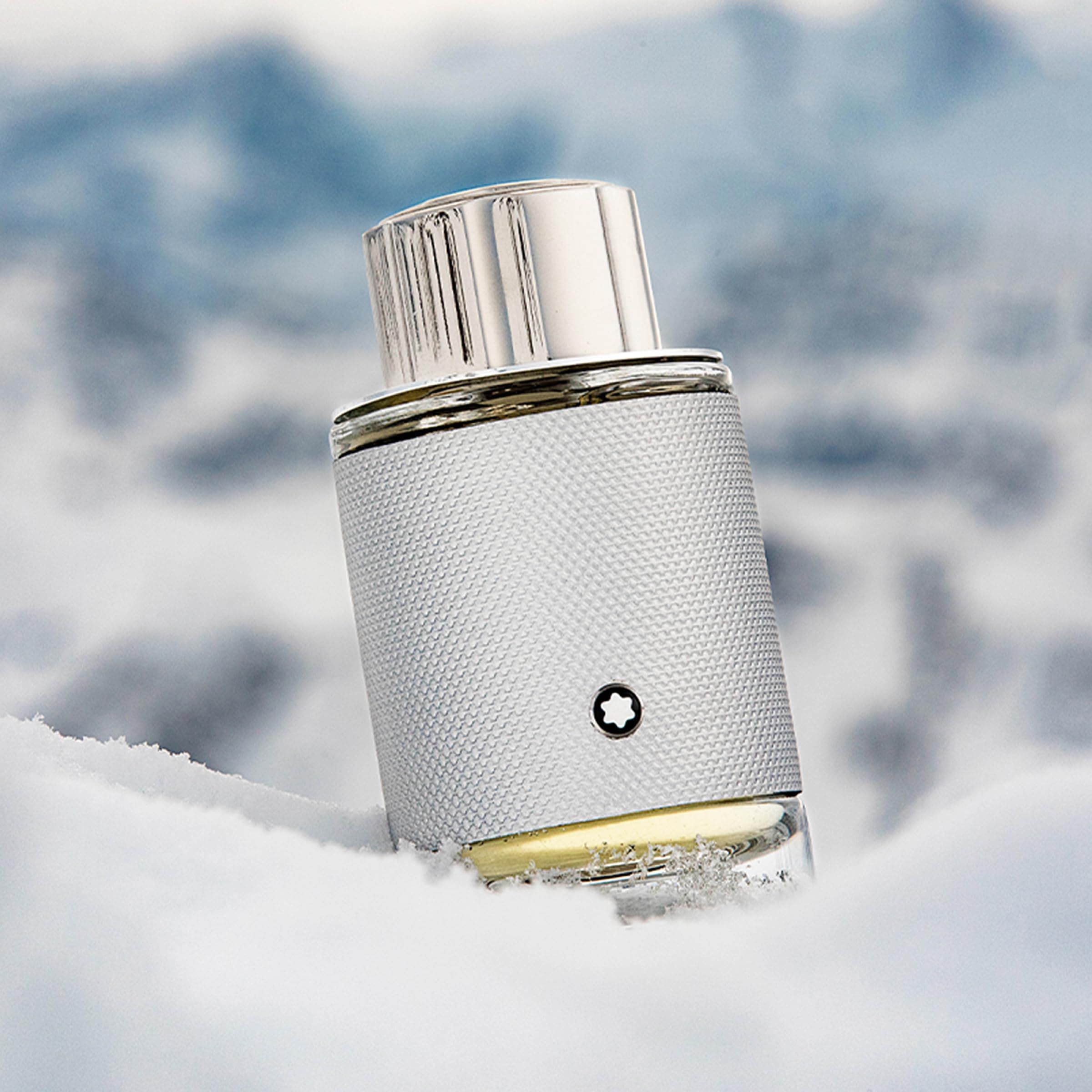 Montblanc Explorer Platinum EdP Nat. Spray. Flacon argenté dans la neige. Bouchon argenté et flacon avec logo. Fond : montagnes enneigées.