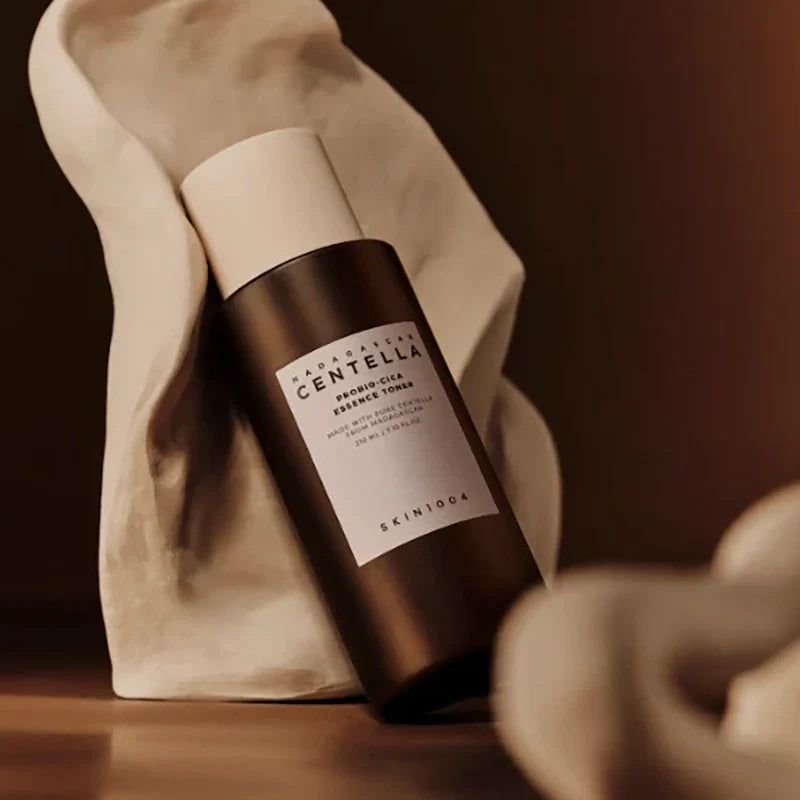 Bruine fles met witte dop, voor witte stof. Tekst: MADAGASCAR CENTELLA, PROBIO-CICA Essence Toner, SKIN1004.