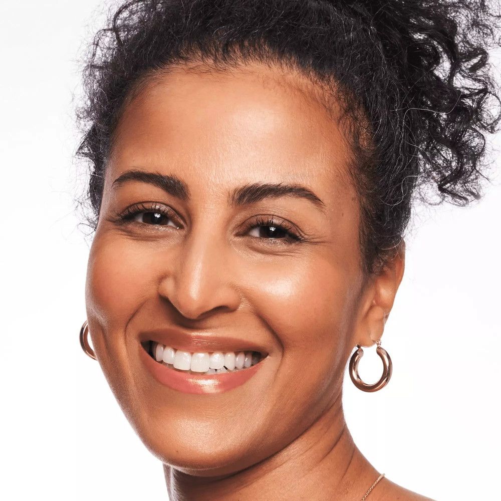 Portret van een vrouw met een gebruinde huid. Ze draagt oorbellen en lacht.
