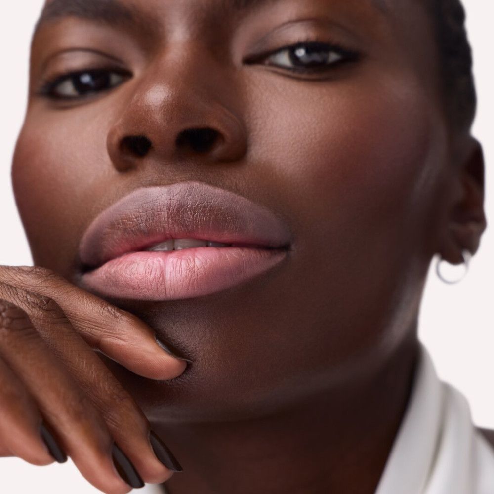 Gros plan sur des lèvres maquillées avec un crayon contour rose. Peau foncée.