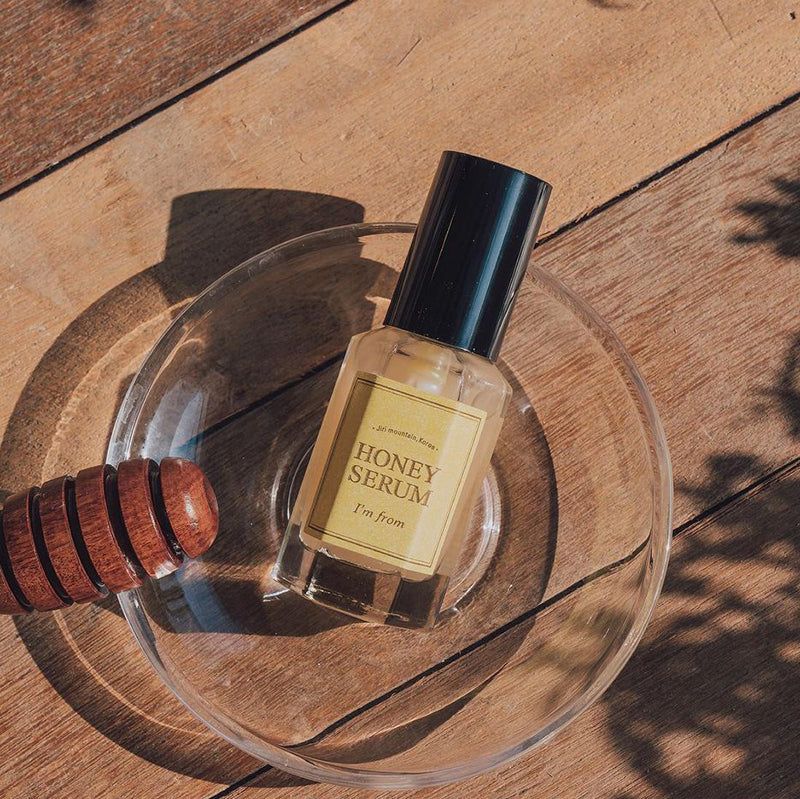 Flacon de sérum dans un bol en verre. Mélangeur à miel à côté. L'étiquette indique "HONEY SERUM" et "I'm from".