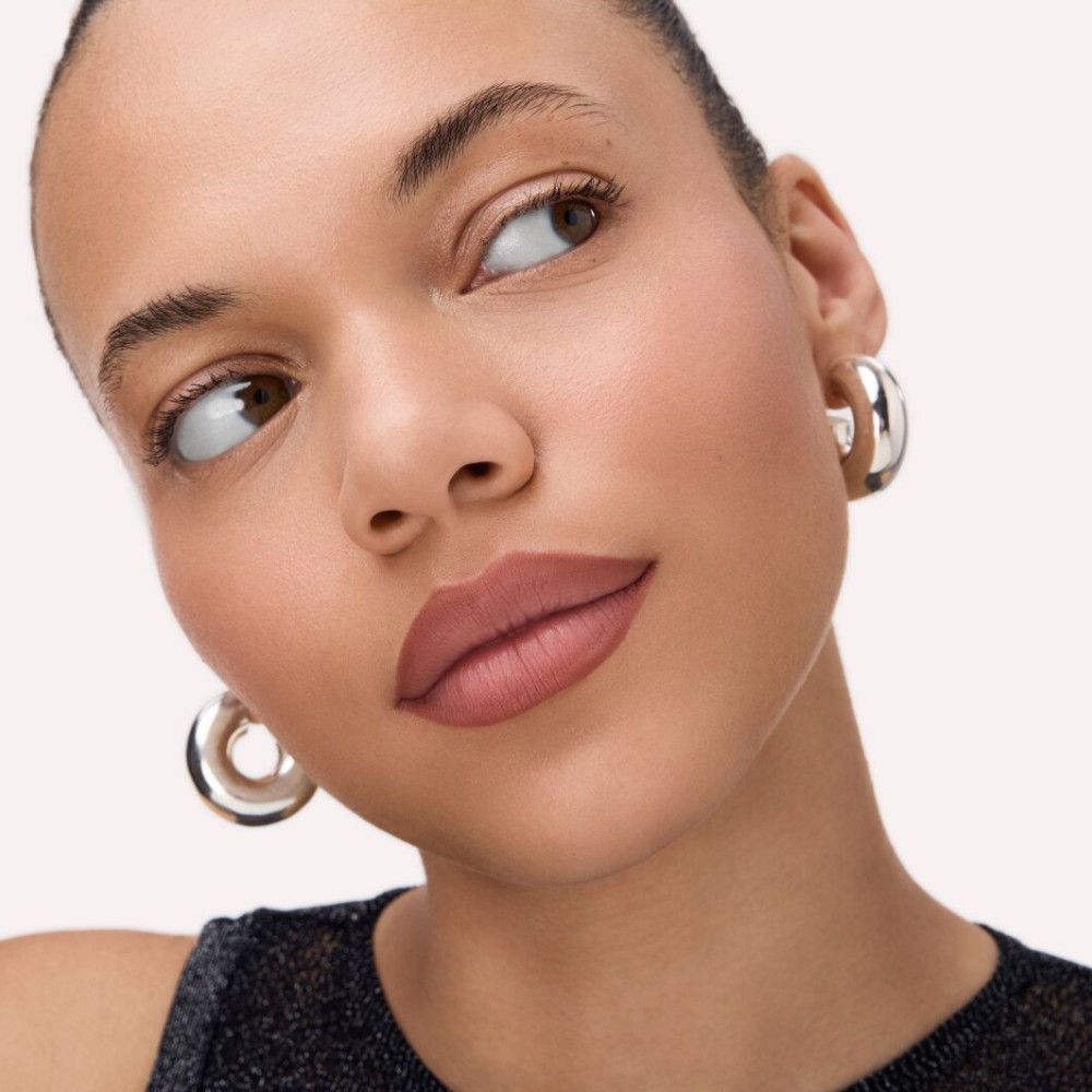 Portrait d'une femme avec des lèvres maquillées. Les lèvres sont remplies d'une teinte marron. La femme porte des boucles d'oreilles argentées.