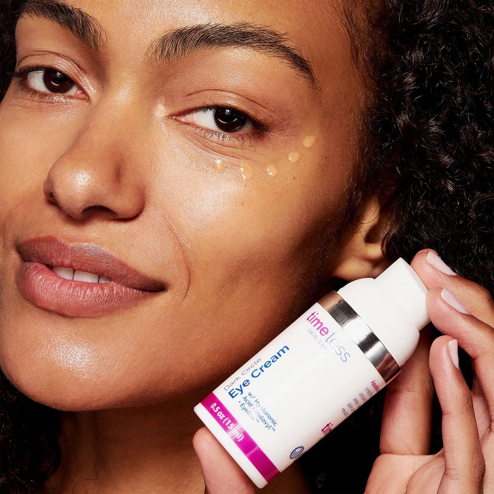 Vrouw houdt een fles vast. Opschrift: TIMELESS SKIN CARE, Dark Circle Eye Cream, 0.5 oz (15 ml). Gel op de huid.