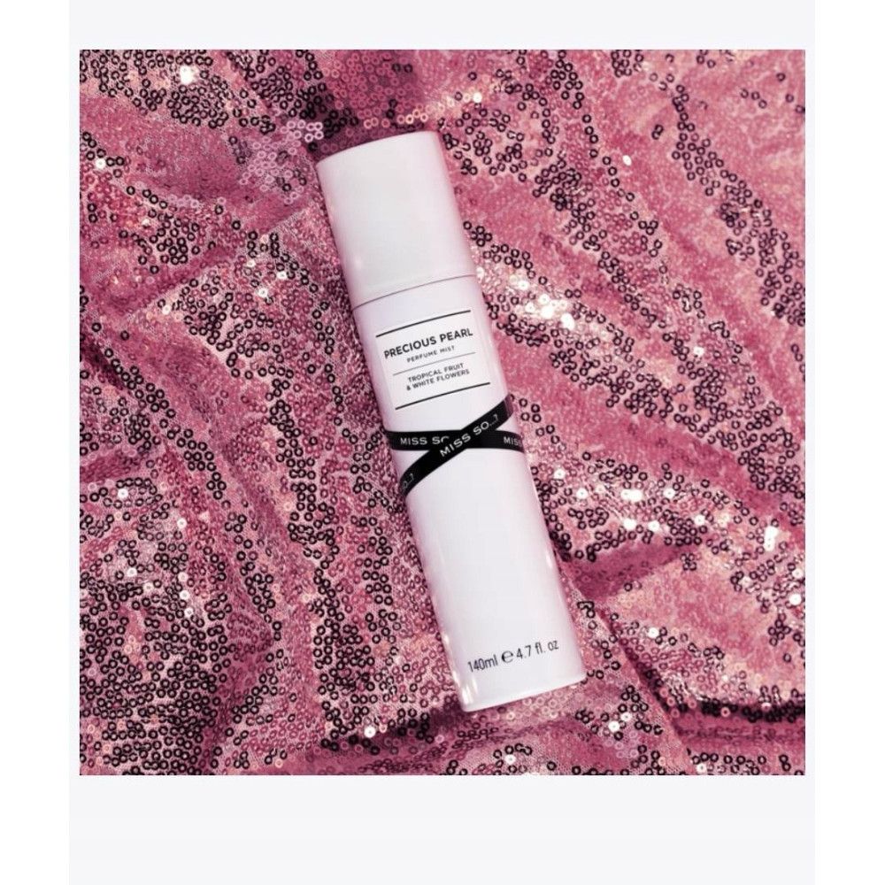 Witte cilindrische fles. Label: Precious Pearl, Tropical Fruit & White Flowers. Zwart lint Miss So. Op roze paillettenstof.