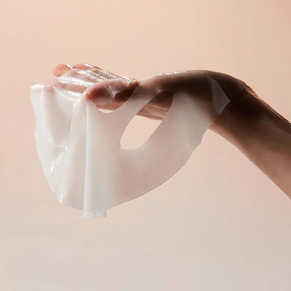 Une main tient un masque facial blanc et humide. Le masque est transparent et comporte des ouvertures pour les yeux et la bouche.