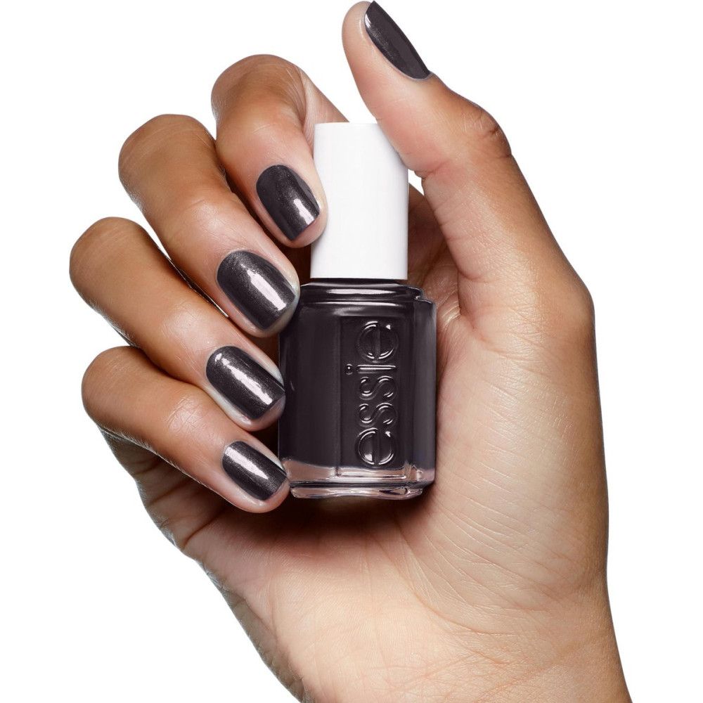 Hand houdt een flesje Essie nagellak vast. Nagels en lak zijn donkergrijs. Essie staat op de fles.