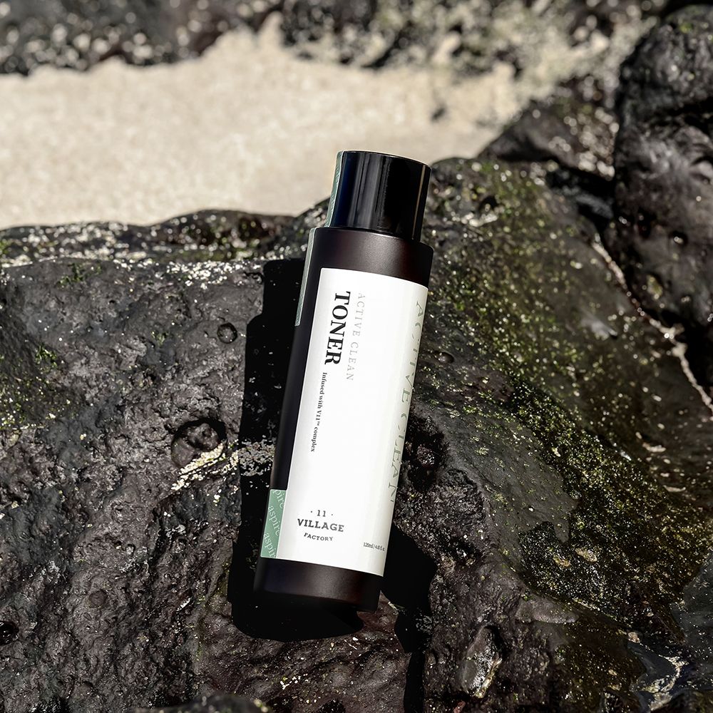 Flacon marron avec bouchon noir sur rochers. Inscription: ACTIVE CLEAN TONER. Marque: VILLAGE 11 FACTORY.