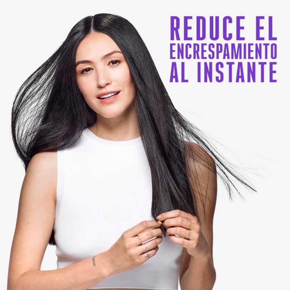 Femme aux longs cheveux noirs. Texte : Réduit les frisottis instantanément. Elle tient ses cheveux.