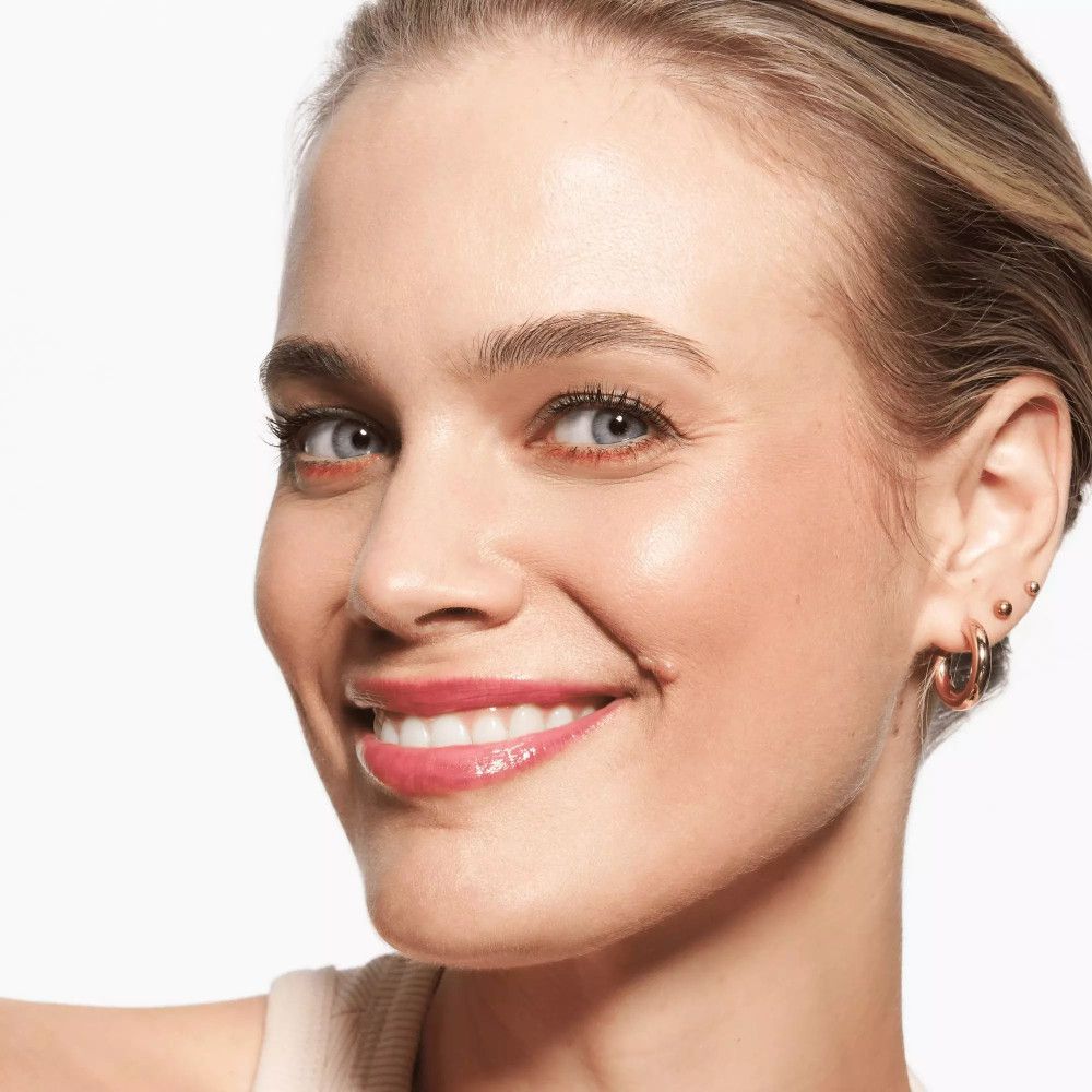 Gros plan d'une femme avec trait de khôl et rouge à lèvres rose. Elle sourit.