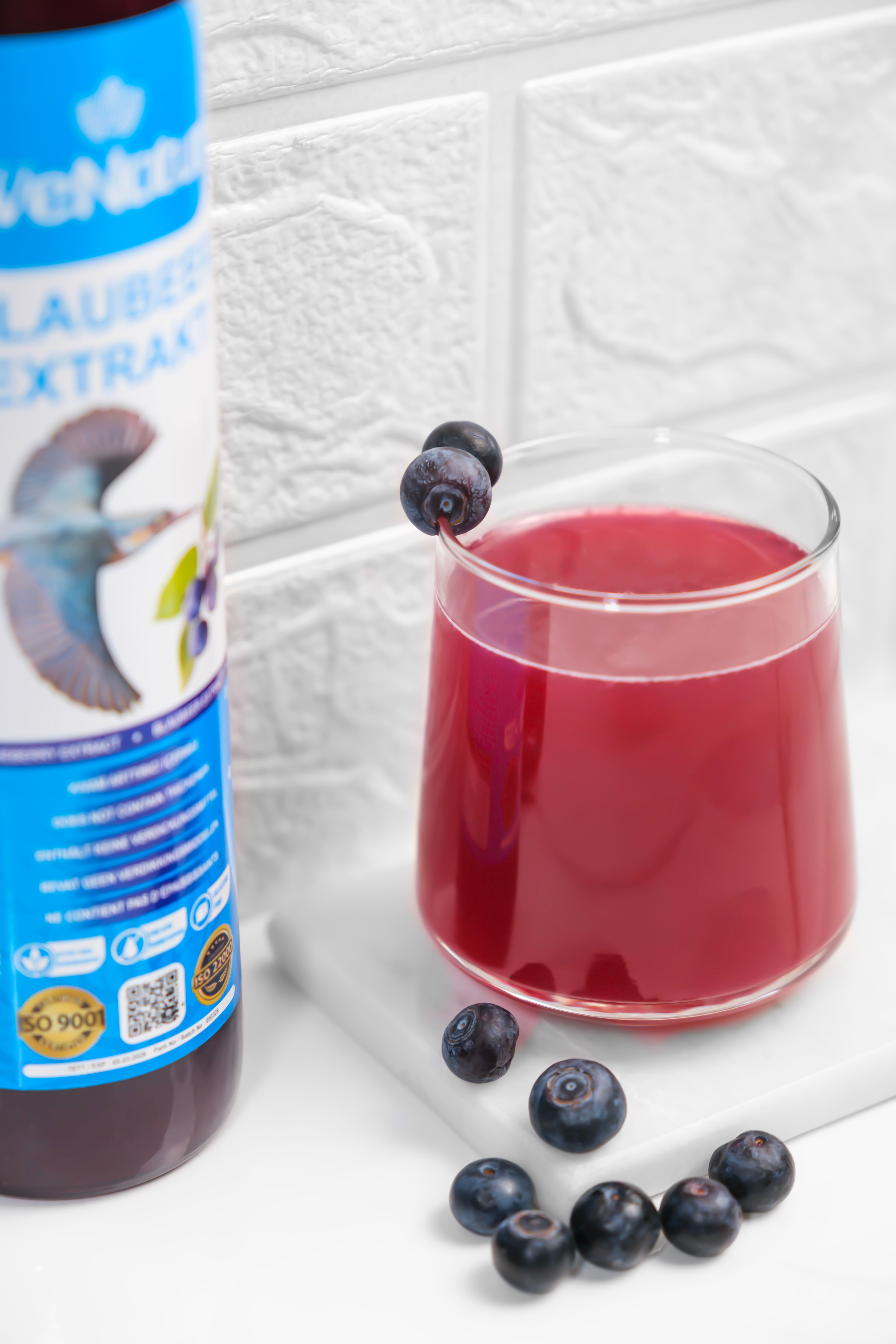 Fles met bosbessenextract en een glas van de drank, gegarneerd met bosbessen. ISO 9001 certificering zichtbaar.