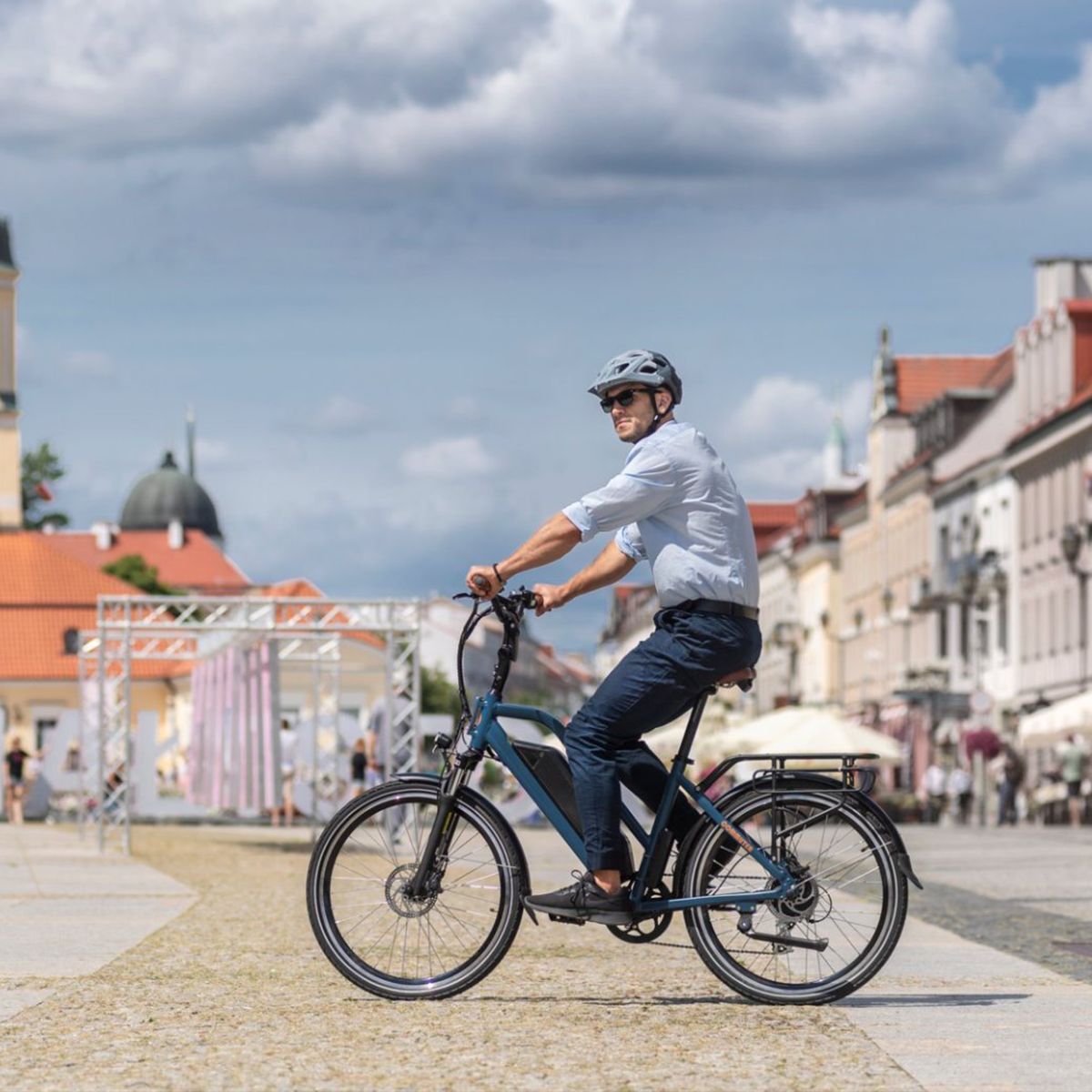 Homme faisant du vélo électrique bleu en ville. Casque, lunettes de soleil.