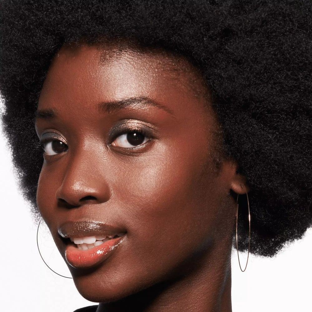 Femme aux lèvres brillantes. Peau foncée, cheveux afro. Créoles dorées.