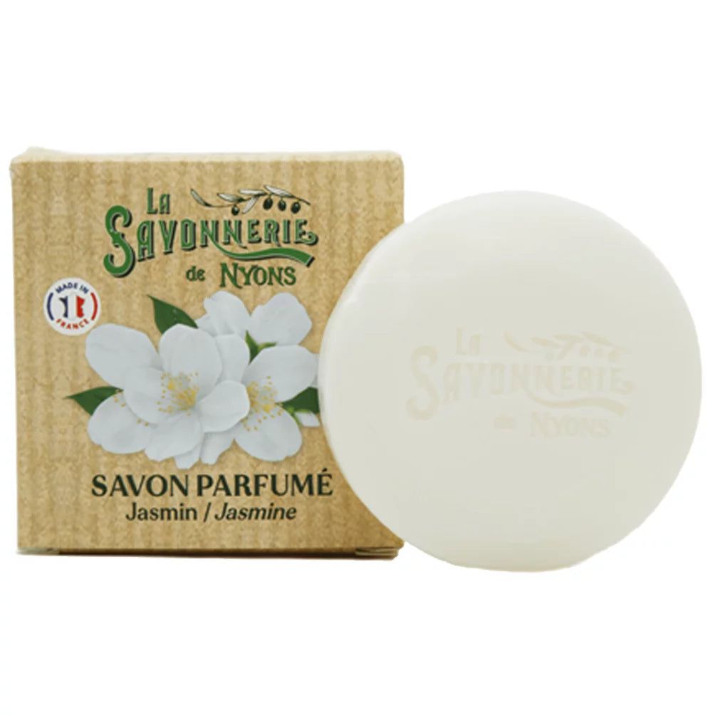 Ronde witte zeep en kartonnen verpakking. Op de verpakking: "La Savonnerie de Nyons", jasmijnbloemen en "Savon Parfumé".