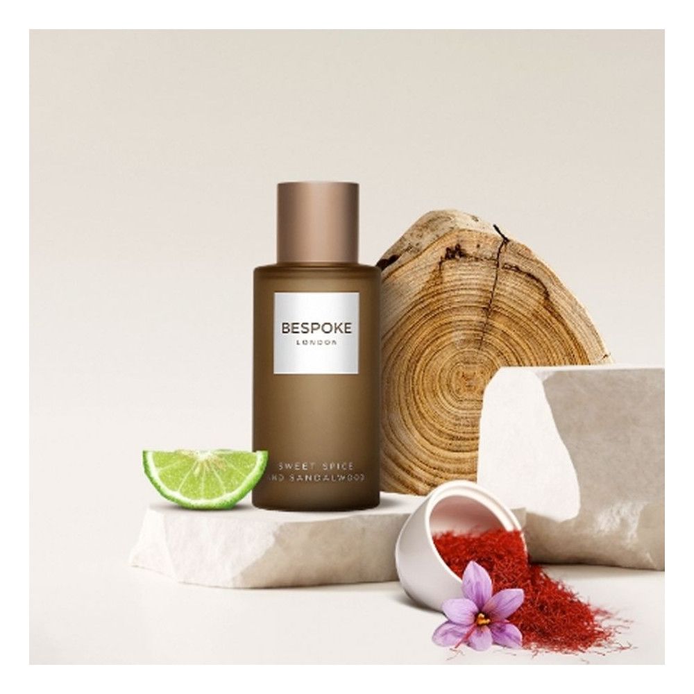 Flacon de parfum avec bouchon cuivré. Étiquette "BESPOKE LONDON". Texte : "Sweet Spice and Sandalwood". Décor : bois, citron vert, épices.