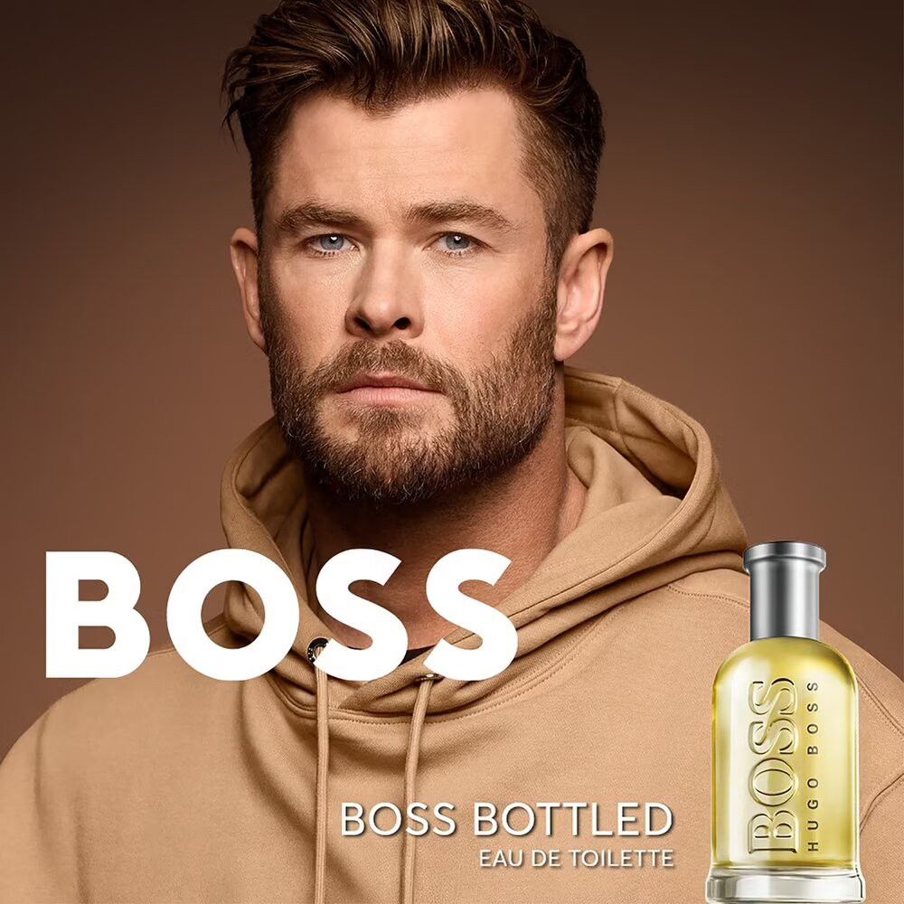 Homme en sweat à capuche et flacon Boss Bottled Eau de Toilette. Nom du produit et logo visibles.