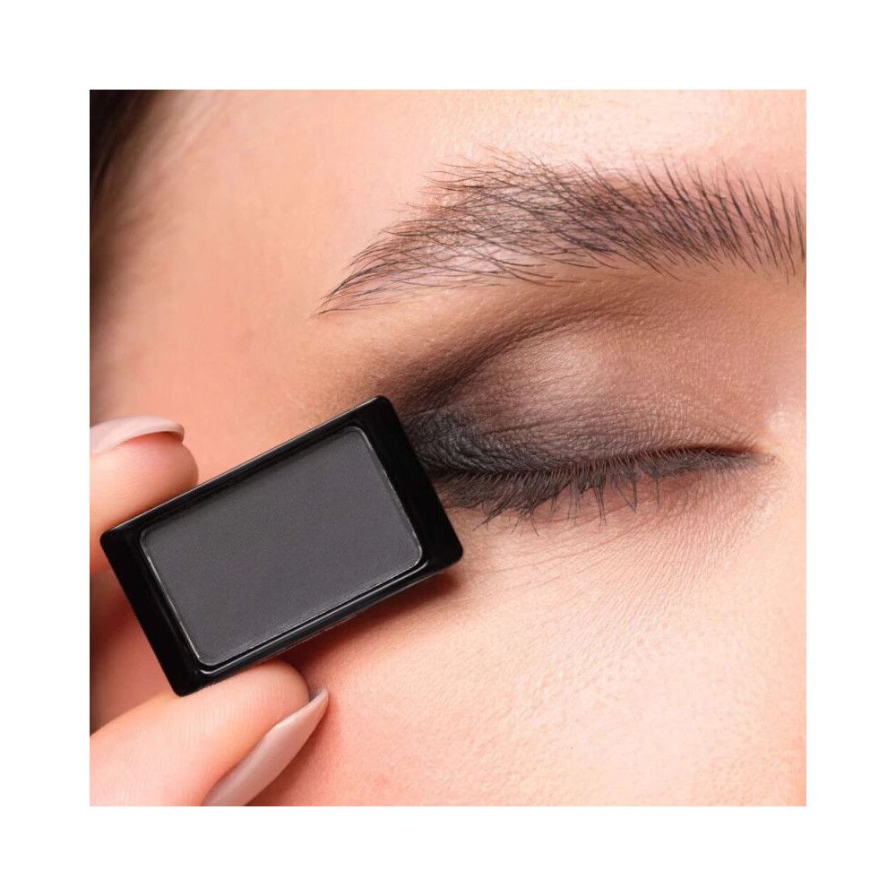 Fard à paupières Artdeco 503 Matt Black. Application sur la paupière. Le produit est tenu par une main. Couleur noire.