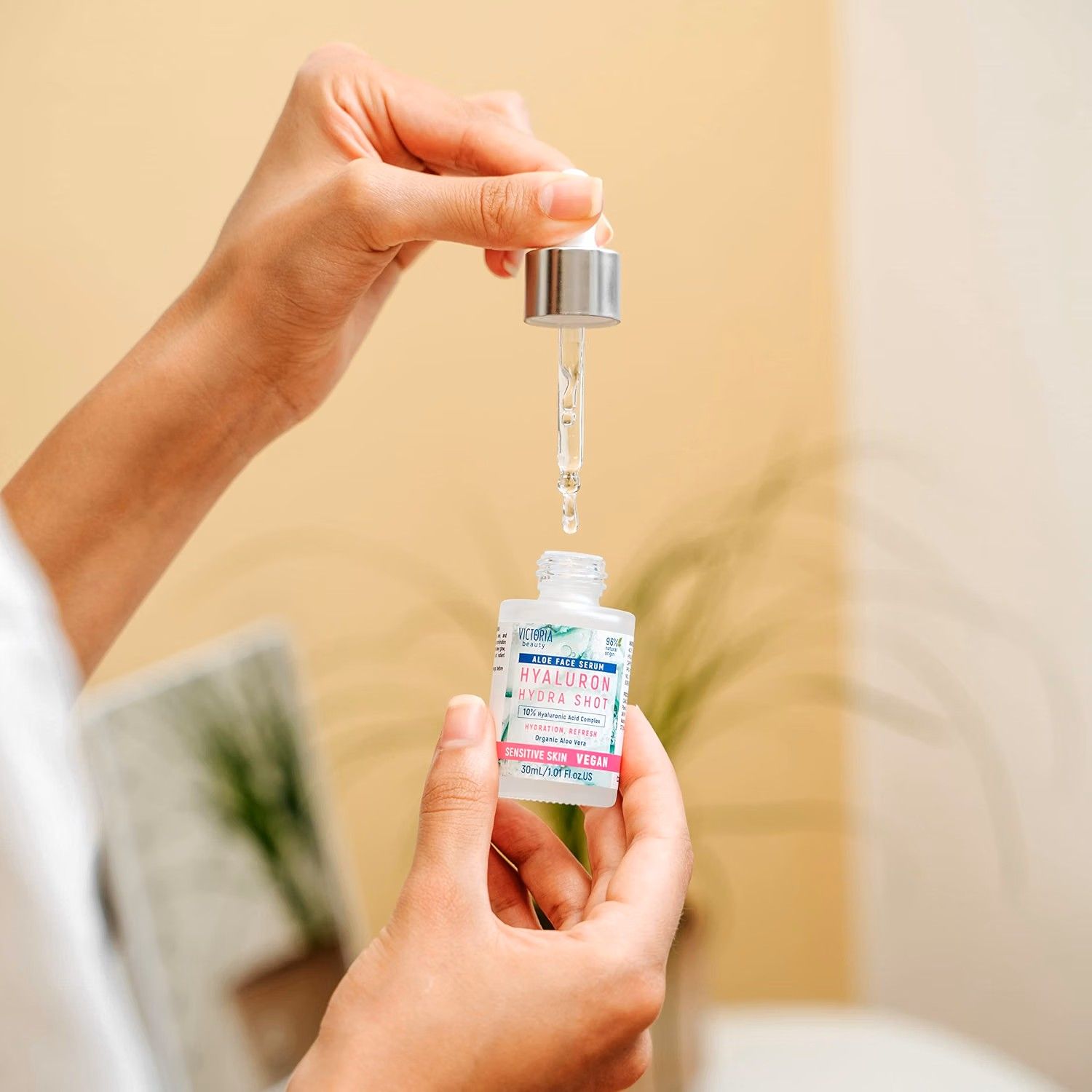 Een hand houdt een klein glazen flesje Hyaluron Hydra Shot serum vast. Een druppelaar geeft vloeistof af.