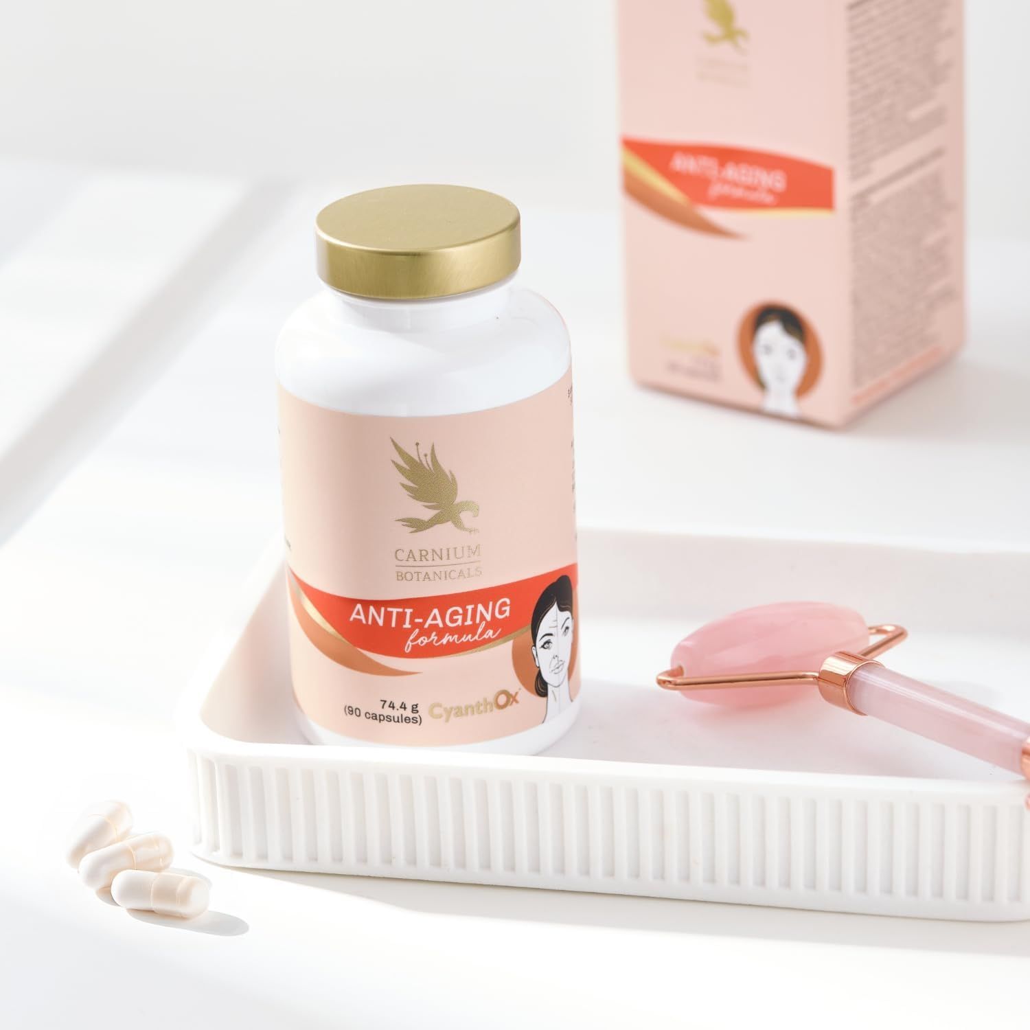 Pilfles met gouden dop in witte schaal. Opschrift: Anti-Aging formula. Rozenkwartsroller ernaast.