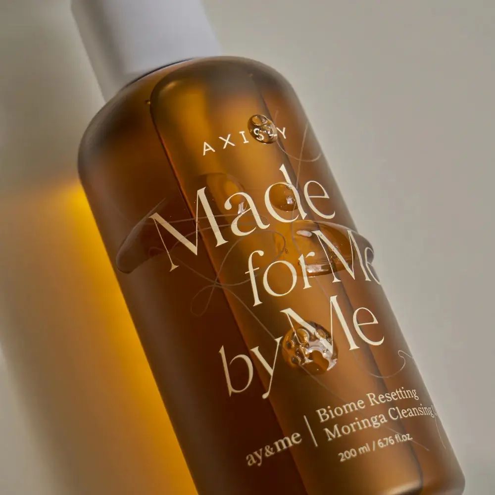 Close-up van bruine fles met witte dop. Opschrift: AXIS-Y, Made for Me by Me, Biome Resetting Moringa Cleansing Oil.