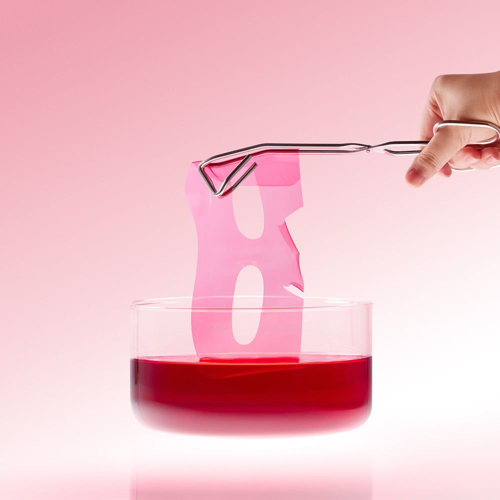 Roze hydrogelmasker wordt met een pincet uit rode vloeistof getild.