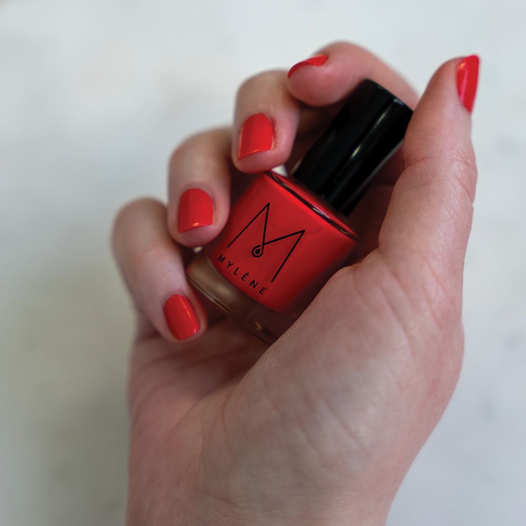 Main tenant un flacon de vernis à ongles rouge. Ongles vernis en rouge. Flacon Mylène.