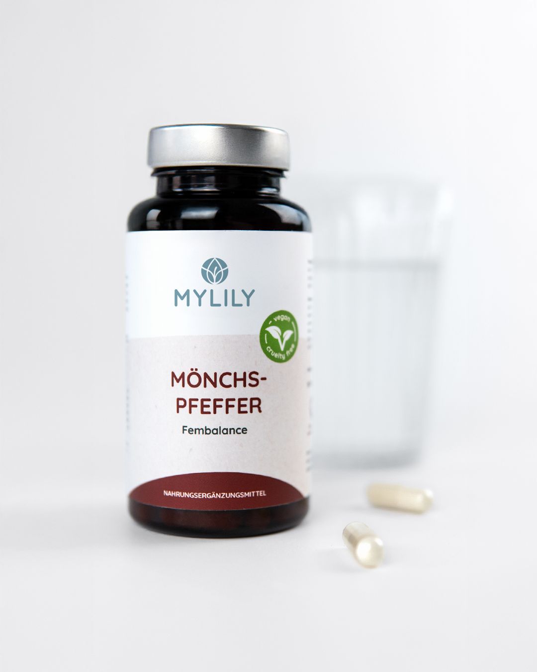 Complément alimentaire Mylily Mönchspfeffer Fembalance dans une bouteille foncée avec un bouchon argenté. Deux gélules sont à côté.