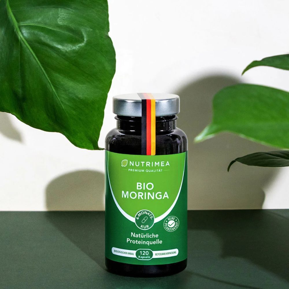 Donkere fles BIO Moringa capsules, 120 stuks. Met bladeren op de achtergrond.