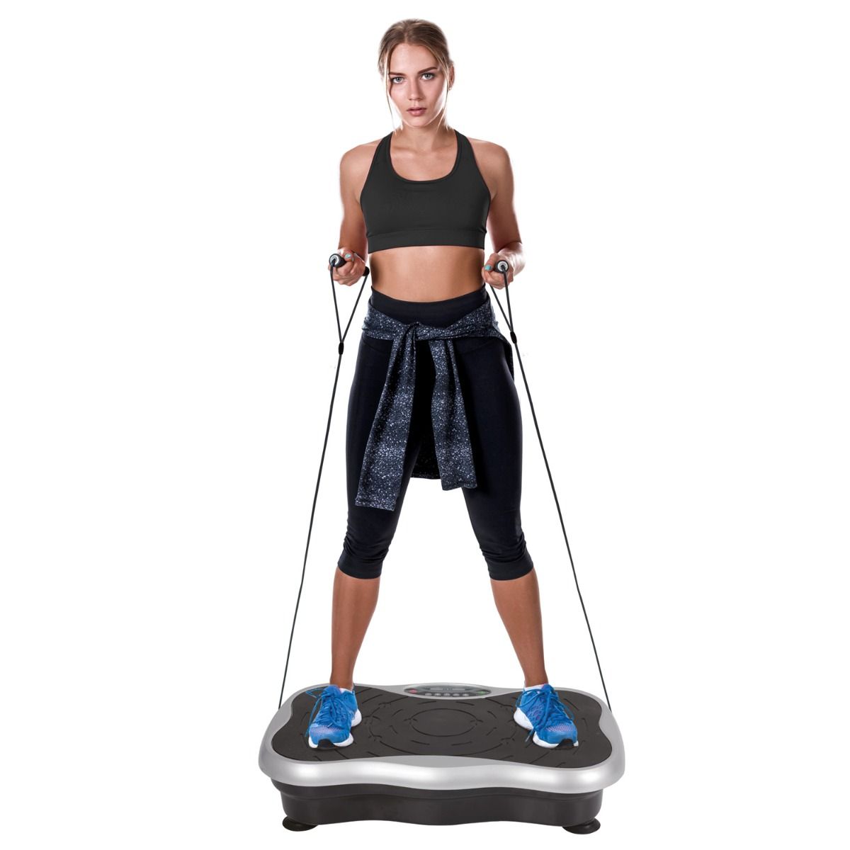 Une femme debout sur une plateforme vibrante, tenant des bandes d'exercice. La plateforme est argentée et noire.