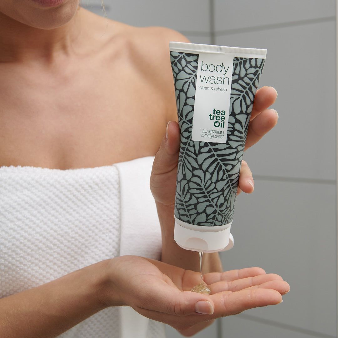Personne tenant un tube de Body Wash. Le produit est versé sur la paume. Marque : Australian Bodycare. Contexte : salle de bain.