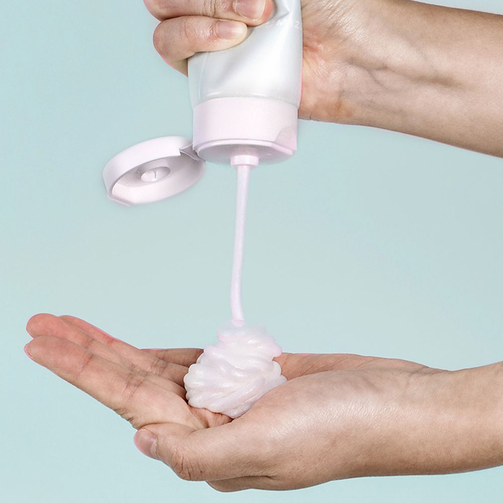 Handen houden een tube en persen schuim eruit. Roze schuim. Witte sluiting. Groen-witte tube.