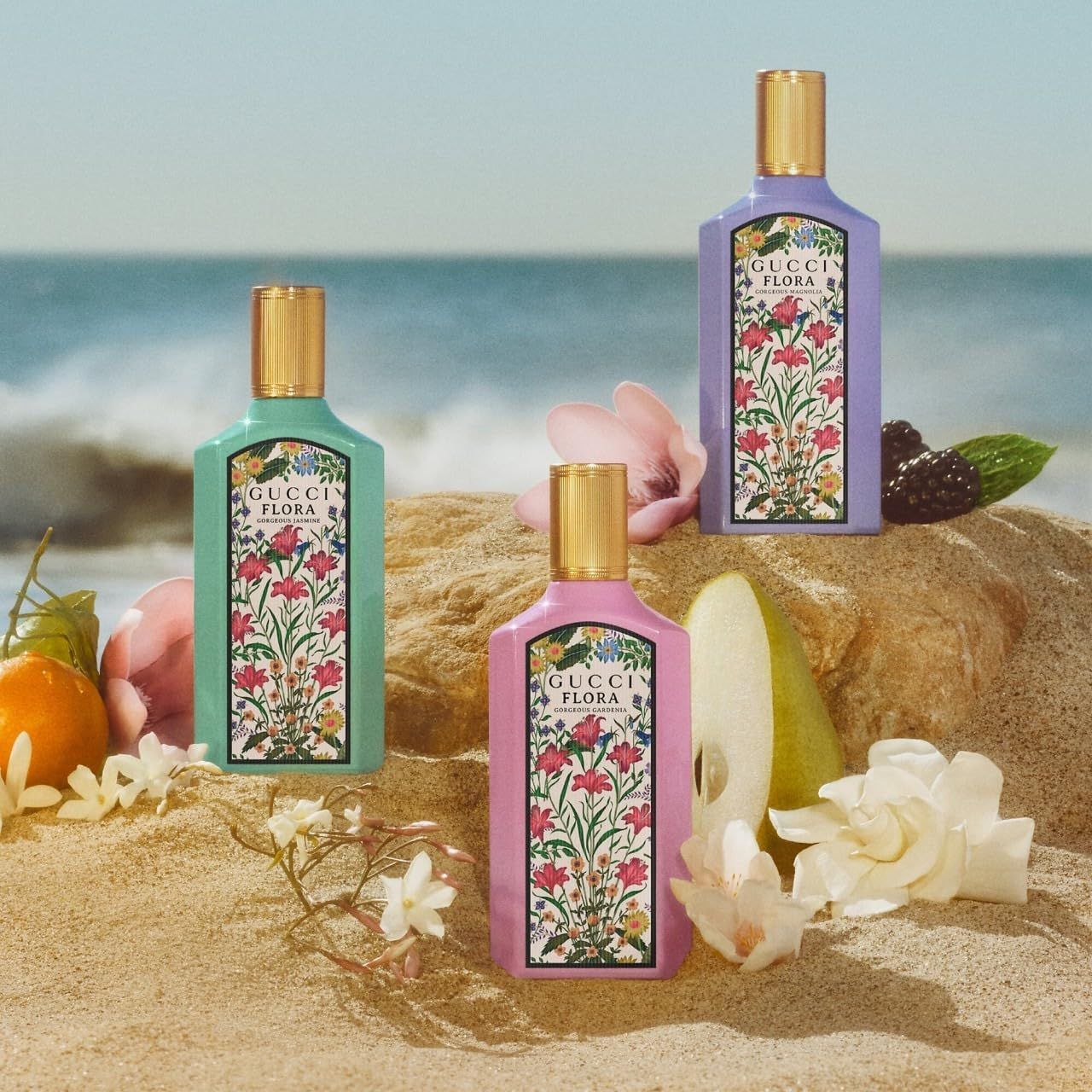 Trois flacons avec étiquettes florales. Bouchons dorés. Inscription : Gucci Flora Gorgeous Magnolia. Fond de plage.