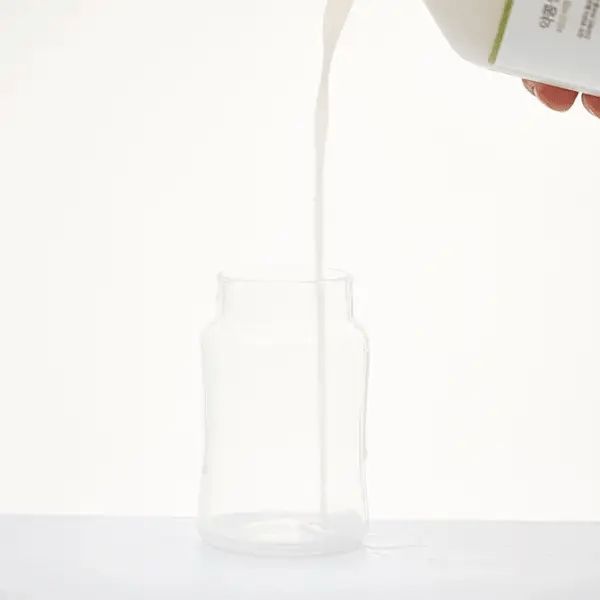 Vloeistof wordt uit een fles in een leeg glas gegoten. Witte achtergrond. Close-up.