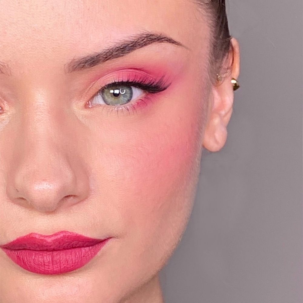 Gros plan d'un visage maquillé en rose. Fard à paupières, blush et rouge à lèvres roses. Œil vert.