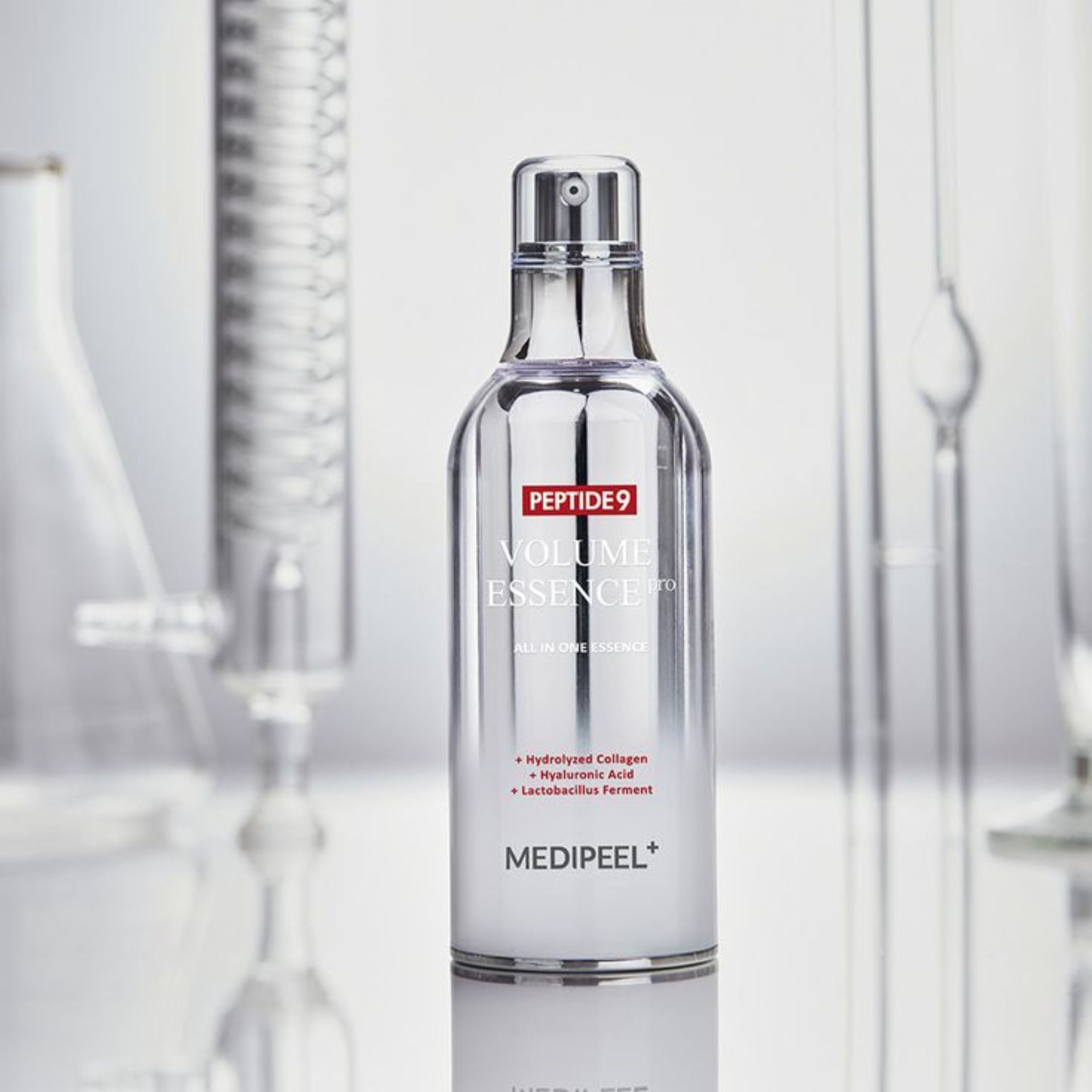 Medi-Peel Peptide 9 Volume Essence dans un flacon argenté, entouré d'équipement de laboratoire. Contient du collagène hydrolysé, de l'acide hyaluronique.