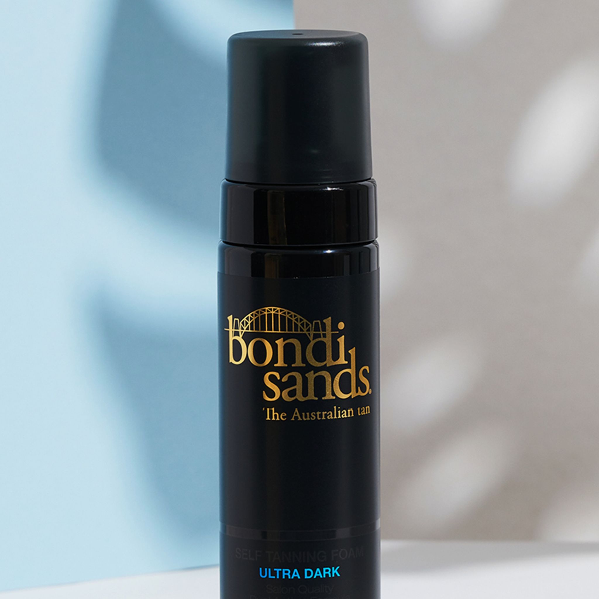 Close-up van een zwarte fles met gouden logo en zwarte sproeikop. Opschrift: Bondi Sands, Ultra Dark zelfbruiningsschuim.