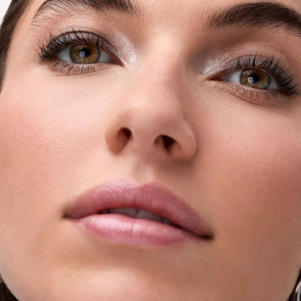 Gros plan d'une femme avec maquillage des yeux. Fard à paupières argenté et gris. Regard ouvert. Fond clair.